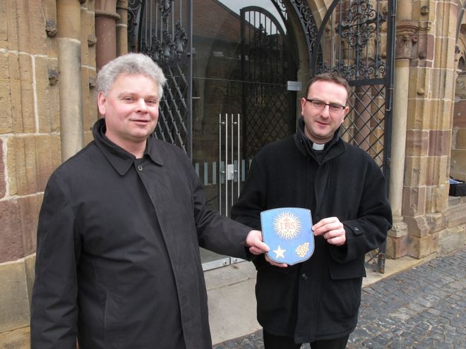 Dechant Jörg-Stefan Schütz und Kaplan Jürgen Kämpf mit dem Wappen von Papst Franziskus, das 20 Minuten später über dem Portal des Fritzlarer Domes hing.